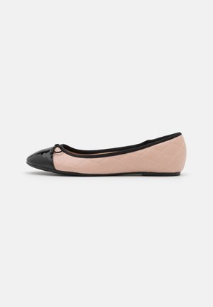 Bailarina acolchada beige con puntera puntiaguda negra brillante, pequeño detalle de lazo y ribete negro alrededor de la apertura.