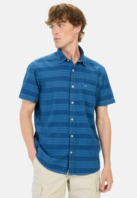 Blå kortærmet skjorte med button-down krave, der har vandrette striber og en brystlomme. Stoffet ser struktureret og letvægtsagtigt ud.