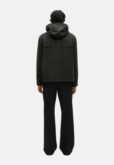 Dunkelgrüne Kapuzenjacke mit lockerer Passform, ausgestattet mit einer glatten Außenstruktur und einem horizontalen Einsatz auf der Rückseite. Kombiniert mit schwarzen Hosen.