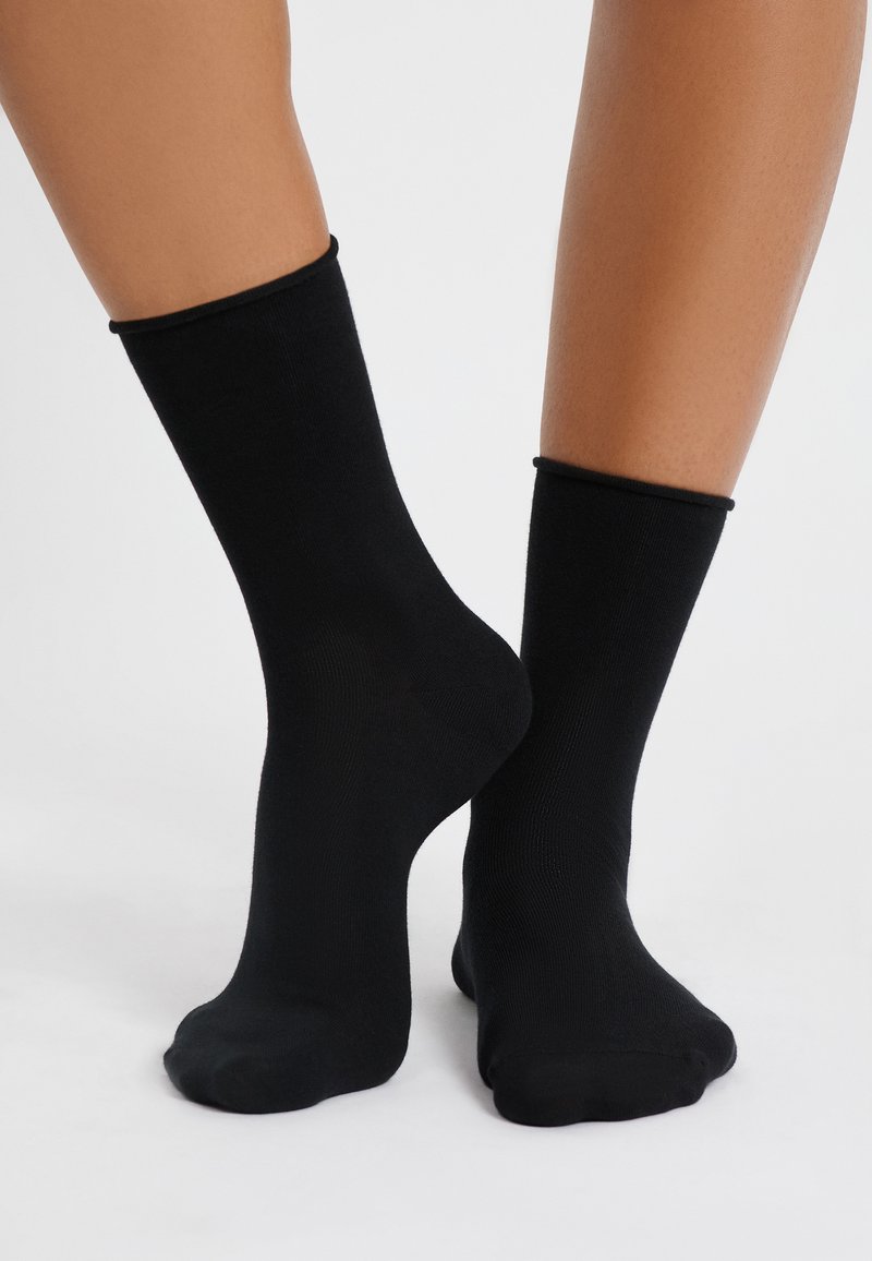 Schwarze Knöchelsocken aus einem glatten, dehnbaren Material. Sie haben ein einfaches Design mit einem gerippten Bund und einer nahtlosen Zehenpartie.