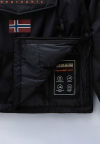Chaqueta impermeable negra con parche de la bandera noruega. En el interior presenta una etiqueta de marca con información sobre el tejido resistente al agua, cortaviento y transpirable.