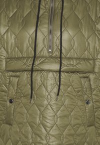 Quiltad olivgrön jacka med halvdragkedja fram, svart dragsko och två tryckknappsfickor. Texturerad diamantmönster över hela ytan.