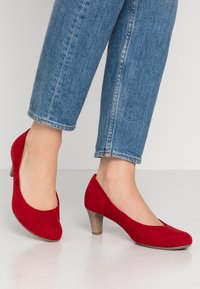 Pompes en daim rouge avec un bout arrondi et un talon bas empilé. Conçues avec une texture lisse et une silhouette classique.