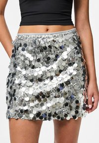 Zilveren pailletten mini rok met een golvende zoom, die het licht weerkaatst met ronde pailletten en een aangesloten taille. Gestructureerd oppervlak.