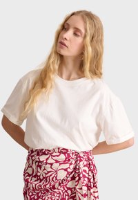 T-shirt bianco in cotone con maniche corte arrotolate, abbinato a una gonna avvolgente a righe rosa e bianca, che presenta disegni floreali.