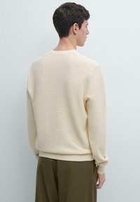 Maglione lavorato a maglia in crema chiaro con motivo a rilievo; presenta una scollatura a girocollo a coste e maniche lunghe, abbinato a pantaloni a taglio morbido.