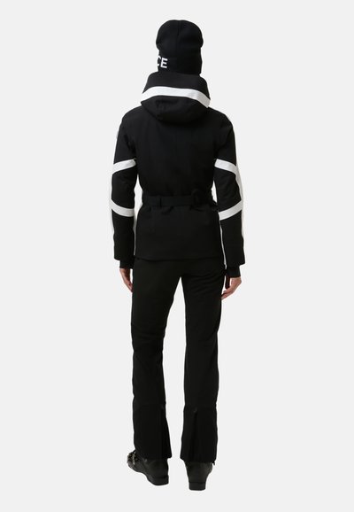 Schwarze Skijacke mit weißen Streifen, taillierte Passform, Kapuze und verstellbarem Gürtel. Kombiniert mit schwarzen Skihosen und Stiefeln, die Reißverschlüsse an den Säumen zeigen.