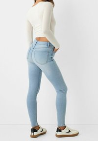 Jasnoniebieskie skinny jeans z dżinsu, z średnim stanem, tylnymi kieszeniami i zwężanym krojem, połączone z białymi trampkami.