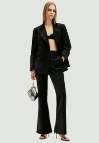 Μαύρο κοστούμι με ρίγες, που περιλαμβάνει κομμένο σακάκι με διπλό μπροστινό και φαρδιά παντελόνια, σε συνδυασμό με ένα cropped τοπ και μια μεταλλική τσάντα.