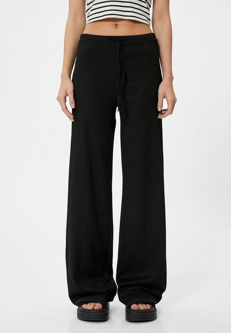 Pantaloni neri a gamba larga con una texture a coste, vita con coulisse elastica e una silhouette fluida, abbinati a calzature chunky con la punta scoperta.