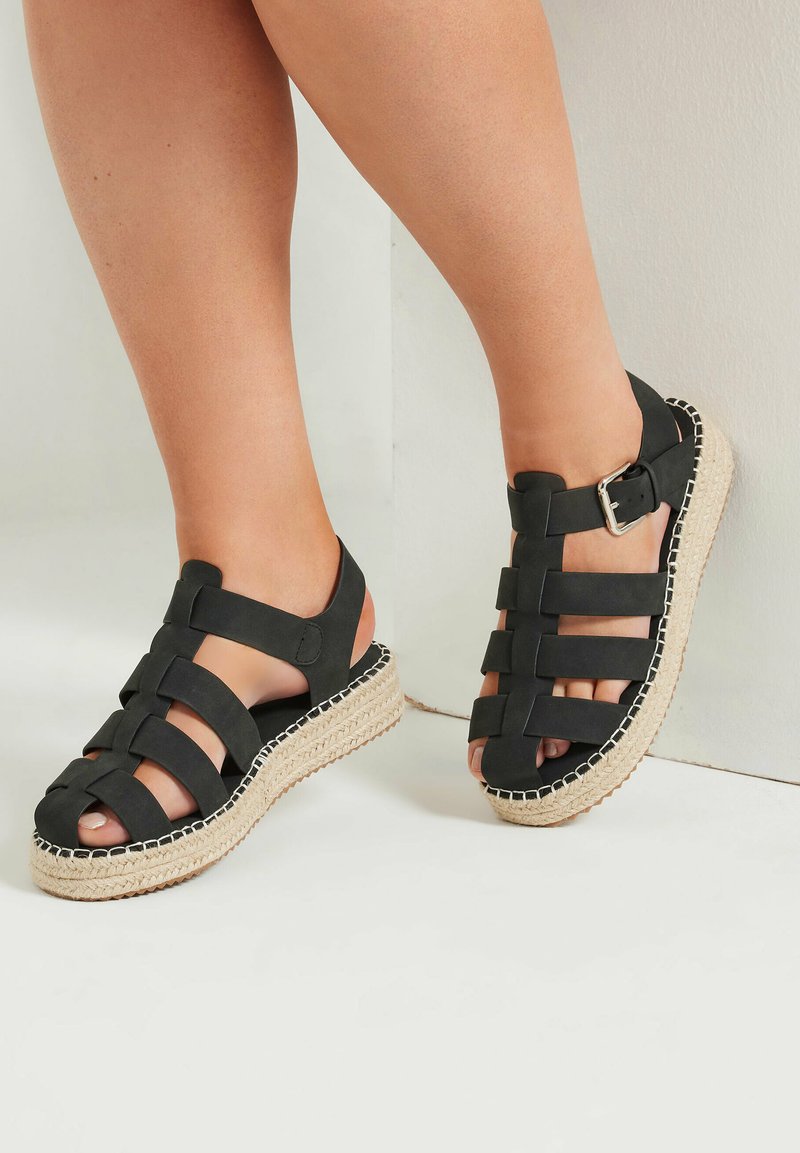 Sandali espadrillas neri con cinturini incrociati, chiusura con fibbia e suola in juta intrecciata. Presentano un design open-toe e una texture opaca liscia.