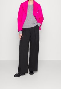 Manteau fuchsia à double boutonnage, pull en tricot gris, pantalon noir à jambes larges et mocassins noirs. Texture lisse, coupe ajustée et couleurs contrastées.