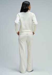 Sudadera blanca y pantalones a juego, hechos de una suave tela, que presentan un corte holgado, puños de canalé y paneles laterales texturizados.