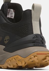 Bota de senderismo negra con parte superior texturizada, suela de goma y acentos beige. Presenta un logo "EXOFRAME" y un detalle "TIMBERGRIP" en la suela.