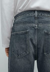 Jeans in denim di un blu scuro sbiadito con una finitura testurizzata. Presenta due tasche posteriori e cuciture a vista lungo la vita.