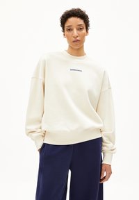Crèmekleurige sweatshirt gemaakt van zacht katoen. Heeft een ronde hals, een oversized pasvorm en een blauw tekstlogo op de borst.