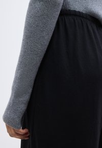 Γκρι ριμπ πλεκτό μπλουζάκι με μακριά μανίκια και εφαρμοστό μανσέτα, συνδυασμένο με φαρδιά μαύρη παντελόνα. Και τα δύο είναι κατασκευασμένα από μαλακά, ελαφριά υφάσματα.