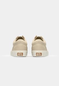 Beige canvas sneakers with rounded heels, white rubber soles, and Vans logo accents on the heel. Simple design with stitching details.