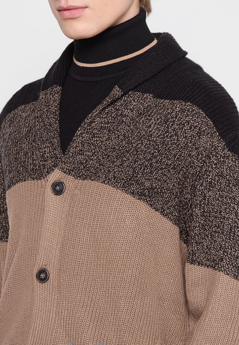 Strickjacke mit einem Schalkragen, der ein strukturiertes Muster in Schwarz, Braun und Beige aufweist. Zwei Knöpfe an der Vorderseite. Weiche Stofftextur.