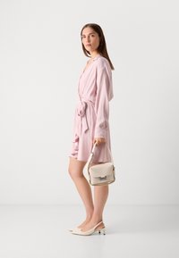 Light pink wrap dress with long sleeves and tie waist, paired with a cream handbag and beige slingback heels with a short block heel.