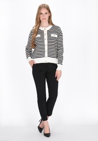 Zwart-witte gestreepte cardigan met ronde hals, knopen aan de voorkant en geribbelde manchetten, gecombineerd met zwarte broek en hoge hakken.