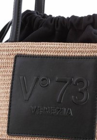 Geweven strohandtas met zwarte leren accenten, voorzien van een textuurlogo en een verzamelde zwarte stofinterieur. Zwarte handvatten bevestigd.