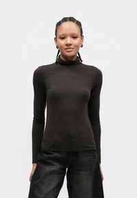 Zwart turtleneck shirt met lange mouwen gemaakt van zachte stof, met een aangesloten design en een gladde textuur, gecombineerd met donkere spijkerbroeken.