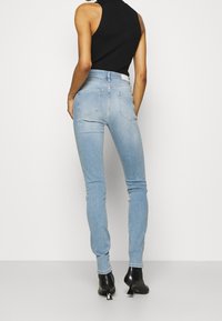 Jeans de mezclilla ajustados de color azul claro con bolsillos traseros, diseño de cintura alta y un ligero estiramiento; llevados con botas de tobillo negras de tacón.
