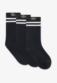 Μαύρες ριγωτές κάλτσες με δύο λευκές ρίγες στην κορυφή, με κεντημένο πράσινο λογότυπο κροκοδείλου. Περιλαμβάνονται τρία ζευγάρια.