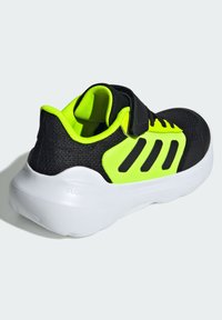 Schwarzer Sportschuh mit neon-gelben Akzenten, Obermaterial aus Mesh, verstellbarem Riemen und einer weißen Gummisohle, die "CLOUDfoam" beschriftet ist.