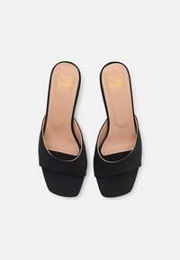 Fekete slip-on szandál sima anyagú felsőrésszel és széles pántos dizájnnal. A talpbetét barna, sárga szív logóval, négyzet alakú orral.