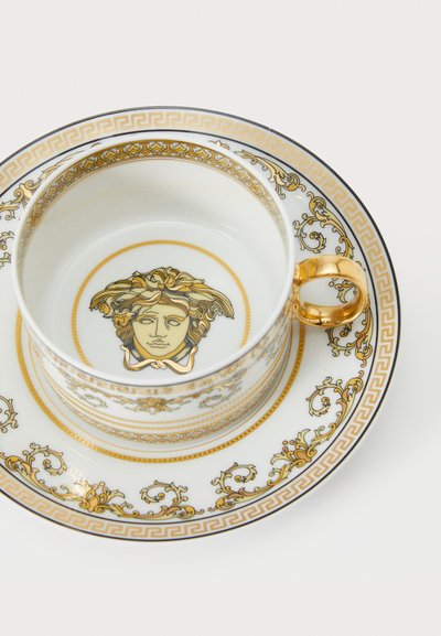 Πορσελάνινη κούπα και πιατάκι, λευκά με χρυσές και μαύρες λεπτομέρειες. Διαθέτουν κεντρικό σχέδιο με Μέδουσα, περίτεχνα χρυσά μοτίβα και χρυσή λαβή.