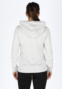 Pullover bianco con cappuccio realizzato in morbido tessuto, con maniche lunghe, tasca a marsupio e discreto logo "SWEDEMOUNT" vicino all'orlo.