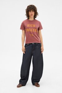 Dark blue wide-leg jeans with a textured finish, paired with a faded red graphic t-shirt featuring yellow lettering and a round neckline.