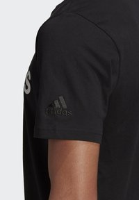 Musta puuvillapaita, jossa on painettu logo edessä ja brodeerattu Adidas-logo hihassa. Lyhythihainen malli, pehmeä rakenne.