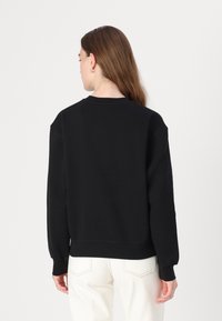 Felpa nera con vestibilità comoda, scollatura rotonda, spalle basse e polsini a coste. Abbinata a jeans bianchi dalla texture.