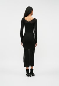 Czarna sukienka z długim rękawem o dopasowanym kroju, z przezroczystą tylną częścią i długości do połowy łydki. Teksturowana tkanina o gładkim wykończeniu.
