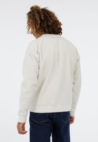 Lichtbeige sweatshirt van een gestructureerd fleece materiaal, met ribgebreide manchetten en een losvallende pasvorm, gecombineerd met donkere denim jeans.