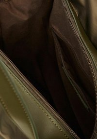 Intérieur d'un sac à main en cuir de couleur vert olive, avec une doublure en tissu marron, plusieurs poches zippées et des côtés lisses et structurés.