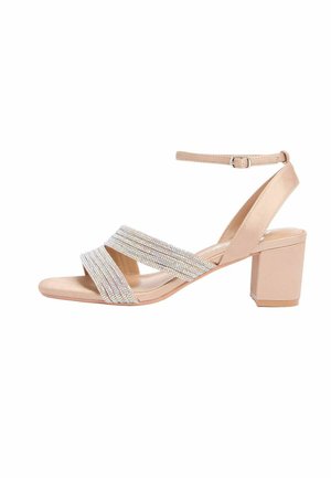 Béžové sandále na blokovom podpätku s remienkom na členku a dvoma trblietavými kryštálmi zdobenými remienkami krížovo cez nohu.