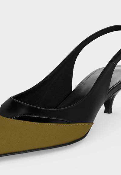 Czarny i oliwkowozielony but na niskim obcasie typu kitten heel, z paskiem na pięcie, z ostrym noskiem i gładką skórzaną powierzchnią na białym tle.