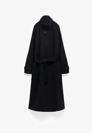 Lange zwarte wollen jas met een hoge kraag, knoopsluiting aan de voorkant en een ceintuur in de taille. Bevat twee grote zakken en knoopmanchetten.