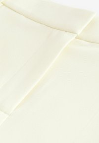 Krämfärgad tyg med en texturerad yta, som har en vikbar krage och släta sömdetaljer.
