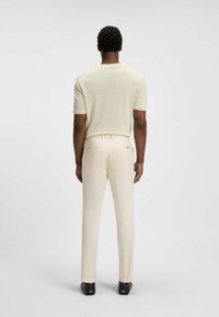 Maglione corto a maniche corte di un beige chiaro con una texture liscia, abbinato a pantaloni aderenti di colore crema con tasche posteriori e un design su misura.