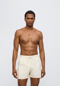 Ανδρικό μπεζ μαγιό σορτς με ελαστική ζώνη μέσης, κορδόνι σύσφιξης και πλαϊνές τσέπες. Ελαφρύ ύφασμα με λεία υφή.
