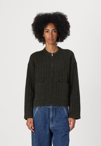 Green ribbed cardigan with a zip front, featuring two front pockets and a relaxed fit, made from textured material.