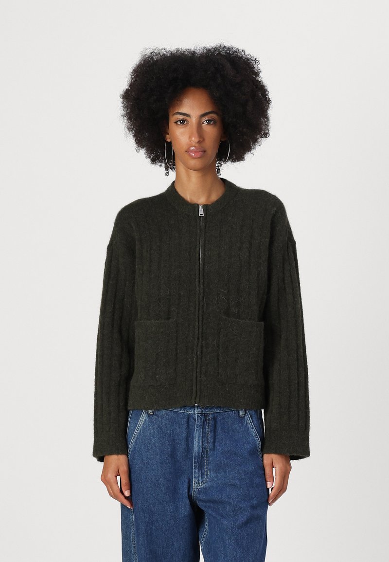 Green ribbed cardigan with a zip front, featuring two front pockets and a relaxed fit, made from textured material.