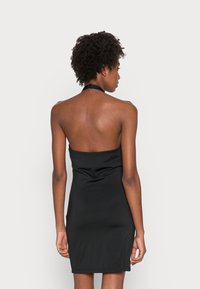 Vestido preto de halter, justo ao corpo com uma textura suave, de comprimento acima do joelho e design minimalista, mostrando os ombros e as costas nus.