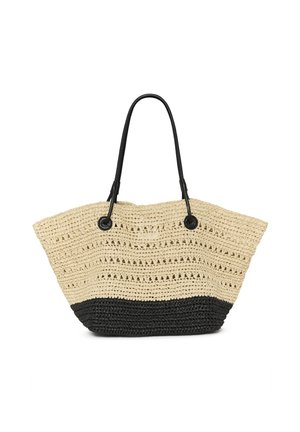 Femme portant de grandes lunettes de soleil et un haut noir sans manches, portant un grand sac à main tissé noir et beige sur l'épaule.