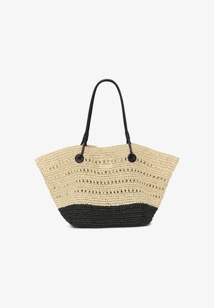 Femme portant de grandes lunettes de soleil et un haut noir sans manches, portant un grand sac à main tissé noir et beige sur l'épaule.